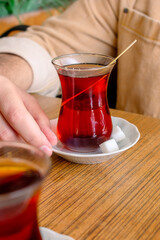 Traditional cup of Turkish black tea. A cup of Turkish tea on a saucer and a piece of sugar. A man is about to drink traditional Turkish tea.