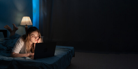 Young woman with laptop computer in bed at home at night. Technology, internet, communication and people concept