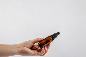 Hand and cosmetic bottles made of dark amber glass on a white background.