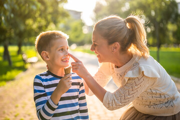 Obraz premium Portrait of happy single mother with her son in park on sunny day. Boys are eating ice cream.