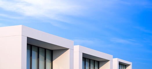 Row of white townhouse buildings with balconies in modern style against blue sky background in...