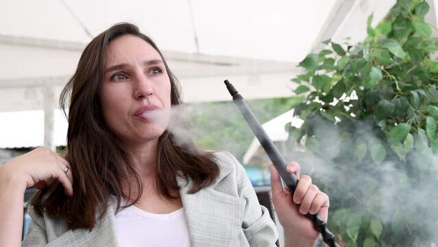 girl woman smoking hookah in terrace restaurant sitting with coffee cup on table,typing message on phone.female with cold sore herpes hpv virus on lips 4k.hookan man putting coal cubes on tabaco bowl