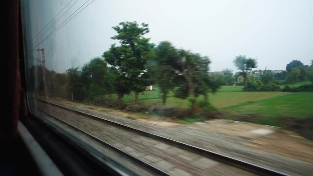Parallel tracks running along a speeding Train with trees and electric poles leaving behind. Northern Indian Railways. India.