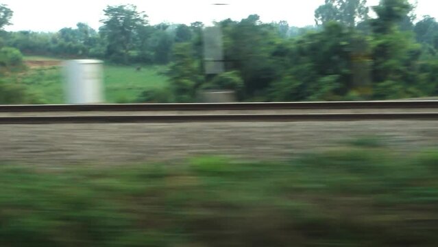 Parallel tracks running along a speeding Train with trees and electric poles leaving behind. Northern Indian Railways. India.