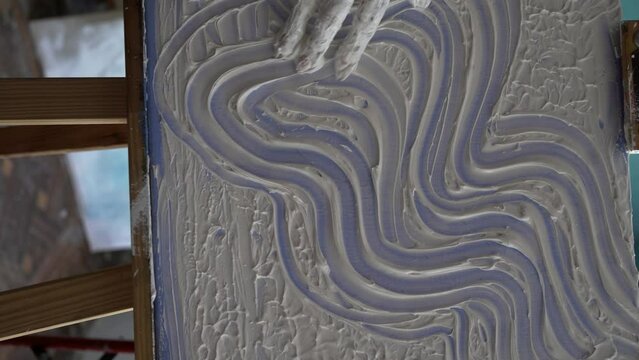 Female artist draws with her hands on the canvas, she creates emotional textured oil painting with fingers. Painter creating abstract modern art.