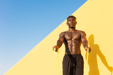 Athletic man training muscles with fitness rubber bands outdoors. Muscular African man with a naked torso exercising..