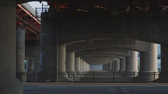 View from Ichon Hangang Park beneath the structured architectural pillars and repeating arches of the Hangang Bridge in Seoul, featuring citizens riding bicycles and jogging along the riverside path.