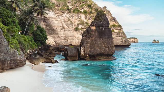 Podr&oacute;żnik idący po pięknej plaży Diamond, na Indonezyjskiej wyspie Nusa Penida, plaża, skały klif oraz ocean.