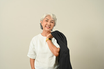 Smiling senior businessman with jacket over shoulder standing isolated on beige background