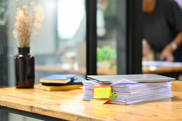 Wooden office desk with pile of documents, laptop and supplies