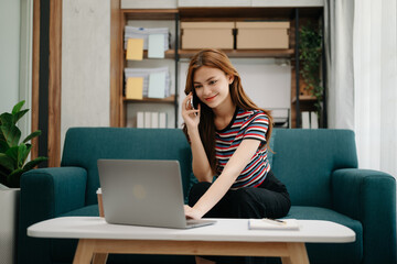 Fototapeta premium Young beautiful woman using laptop and tablet while sitting at her working place. Concentrated at work. in living room on the sofa at home office.