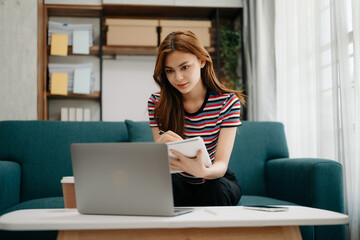 Young beautiful woman using laptop and tablet while sitting at her working place. Concentrated at work. in living room on the sofa at home office.