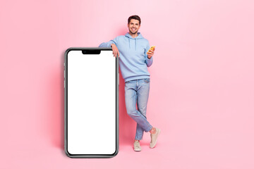 Full body size photo of young attractive brunet hair positive man hold new smartphone empty space banner app isolated on pink color background
