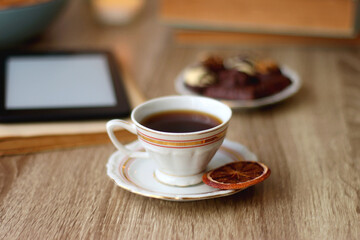 Books, reading glasses, e-reader, plate of chocolate pralines, bowl of cookies, cups of tea and lit candles on the table. Selective focus.