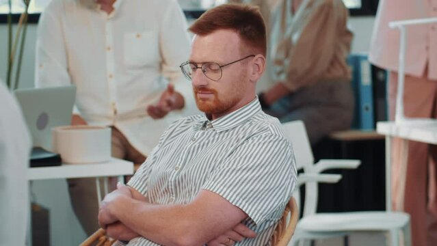 Young male project manager feeling boredom during team meeting in busy office