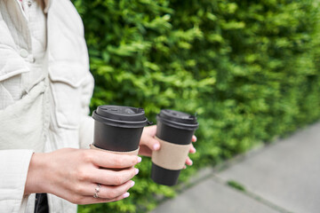 A girl in a residential neighborhood holds cups of coffee. Two glasses of hot drinks in the hands of a young woman. Breakfast on the go. Picnic and going out concept. 