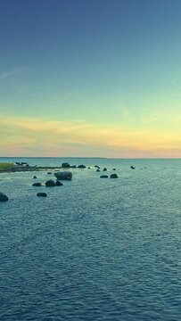 Serene coastal nature, romantic sunset scenery, rippling water and rocks, horizon, vertical short video