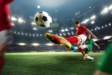 Winning goal. Football players in motion during game at open air 3D stadium with flashlights. Kicking ball in jump. Concept of professional sport, championship, game, achievement, motivation