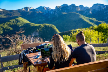 Young couple working remote as digital nomads in the sunshine on a mountain in Montenegro with a...