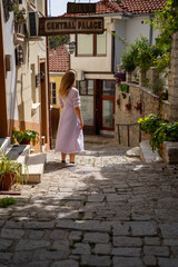 Fototapeta na wymiar Young woman in a pink and purple dress posing in a historic alley in Ohrid, North Macedonia