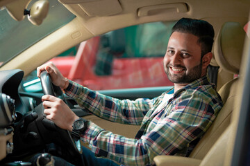Side view of handsome young indian man driving his car and smiling