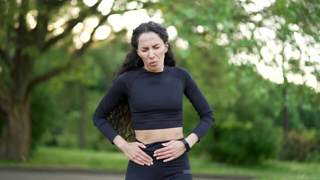 A young sports woman experiences a sharp pain in her right side during a morning run in a park. A female runner in a tracksuit has a liver bolt. The sportswoman gasps in pain, clutching her side
