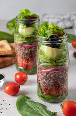 Fototapeta na wymiar Healthy salad with quinoa, avocado, cherry tomato, radish, spinach, and olive oil in a Mason jars on gray background