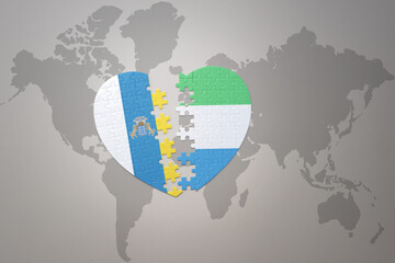 puzzle heart with the national flag of sierra leone and canary islands on a world map background.Concept.