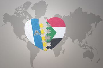 puzzle heart with the national flag of sudan and canary islands on a world map background.Concept.