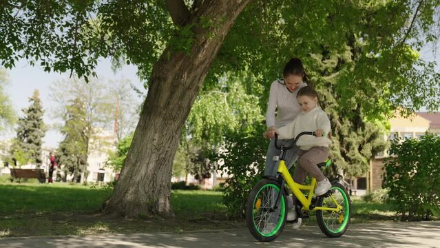child learn ride bike. mother daughter girl drive park. happiness smile little child mom. dream family., girl spins bicycle wheel, mother teaches little smiling child ride bike, having fun with child