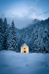 Kirche beleuchtet im Schnee mitten im Wald 