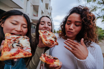 Three multiracial girlfriends having pizza outside