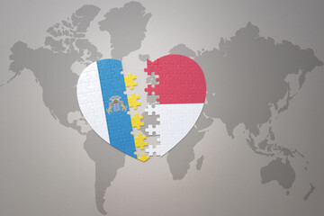 puzzle heart with the national flag of indonesia and canary islands on a world map background.Concept.