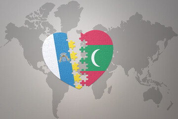puzzle heart with the national flag of maldives and canary islands on a world map background.Concept.