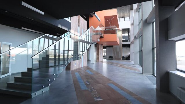 The camera pans across a spacious and empty hall inside a modern office building. The hall is filled with natural light coming through the large panoramic windows, creating an inviting atmosphere