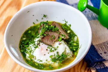 Soup with chicken, spinach and egg in white bowl on a wooden board