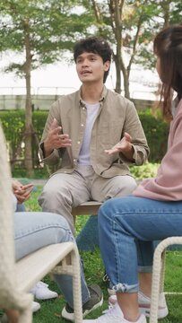Asian group of people sit in a close circle and talk to therapist in park. Smile people sharing story happy speak diverse people in circle at group therapy session with psychologist. Vertical Screen.