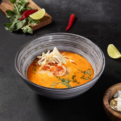 Square frame, side view of a flavorful Tom Yum soup with seafood, lime, and chili peppers, elegantly displayed on a black background