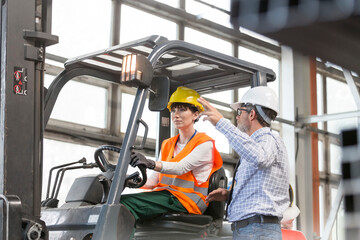 Supervisor directing worker driving forklift in factory - obrazy, fototapety, plakaty