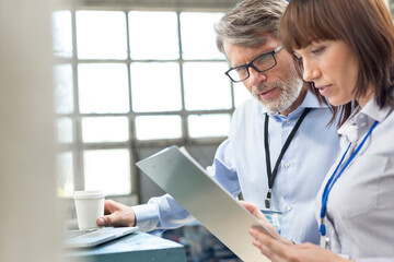 Business people with coffee reviewing clipboard in factory