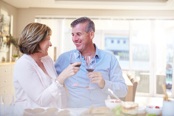 Obraz premium Smiling couple toasting red wine glasses in kitchen