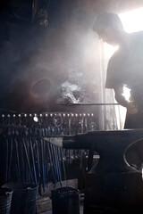 Fototapeta premium Blacksmith holding steaming wrought iron over anvil in forge