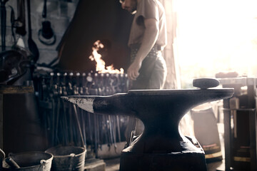 Blacksmith at fire behind anvil in forge