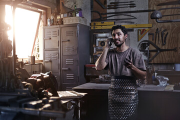 Obraz na płótnie Canvas Blacksmith talking on cell phone in forge