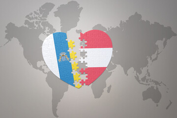 puzzle heart with the national flag of austria and canary islands on a world map background.Concept.