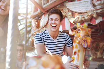 Enthusiastic young man riding carousel at amusement park