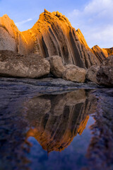 Reflection landscape of a colorful rock formations (Flysch) of the Portio beach at sunset in Cantabria, north of Spain.