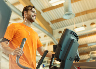 Smiling man with headphones using elliptical trainer at gym
