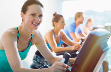 Portrait smiling woman riding exercise bike at gym