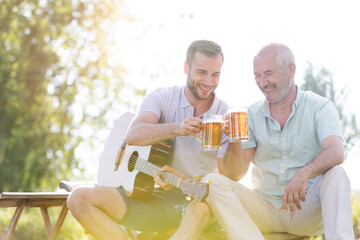 Father and adult son toasting beer mugs and playing guitar outdoors